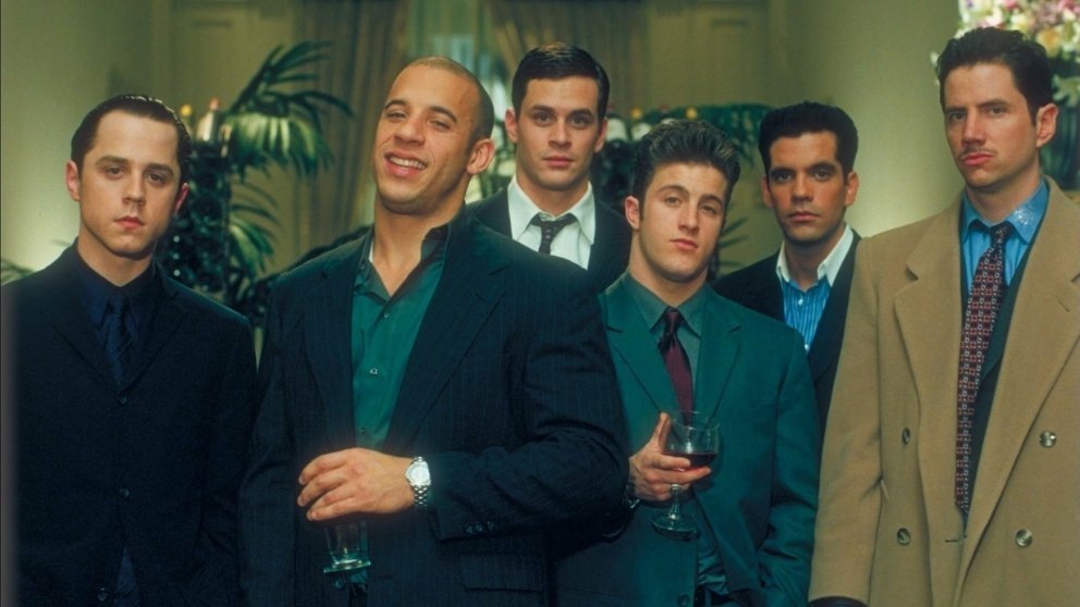 A scene from Boiler Room showing a group of young stockbrokers, with Vin Diesel in the center holding a glass of wine.