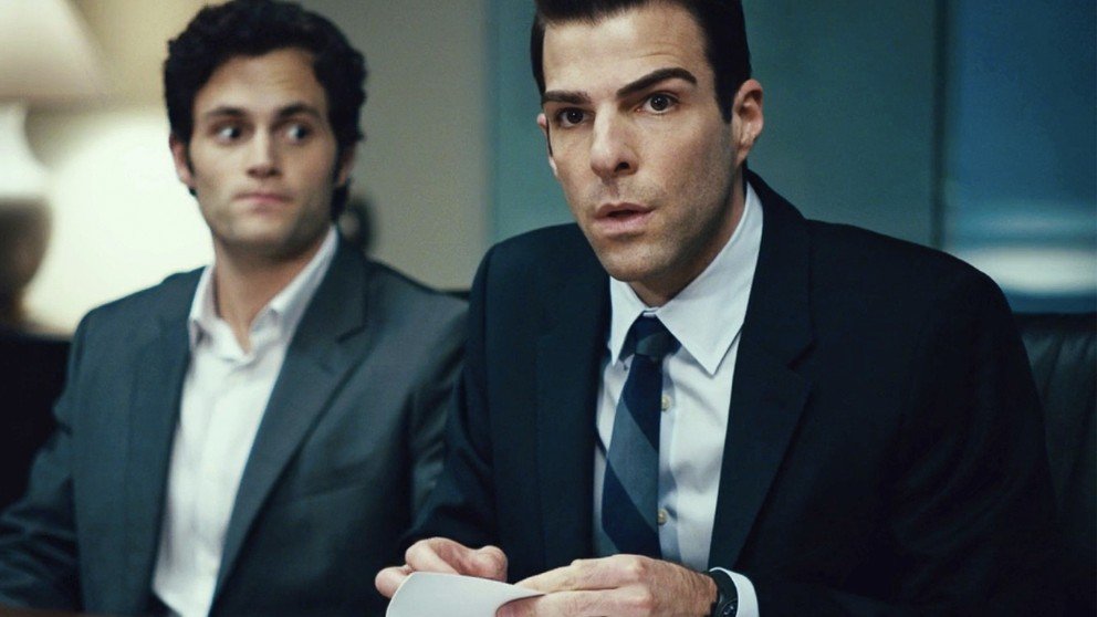 Picture from Margin Call, showing two men in suits at a tense meeting. Zachary Quinto’s character holds a paper, looking concerned.