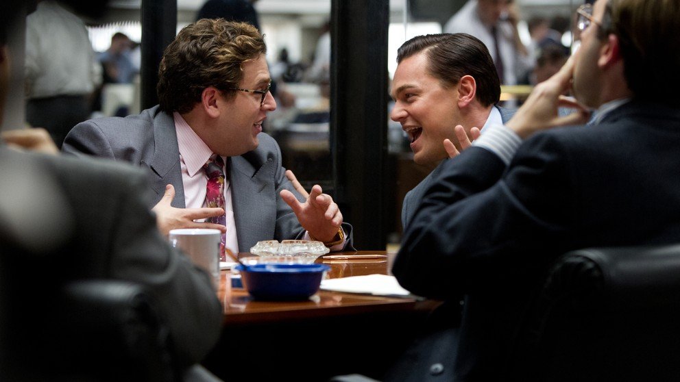 Picture of a busy office scene from The Wolf of Wall Street, where Jordan Belfort and Donnie Azoff are laughing and chatting.